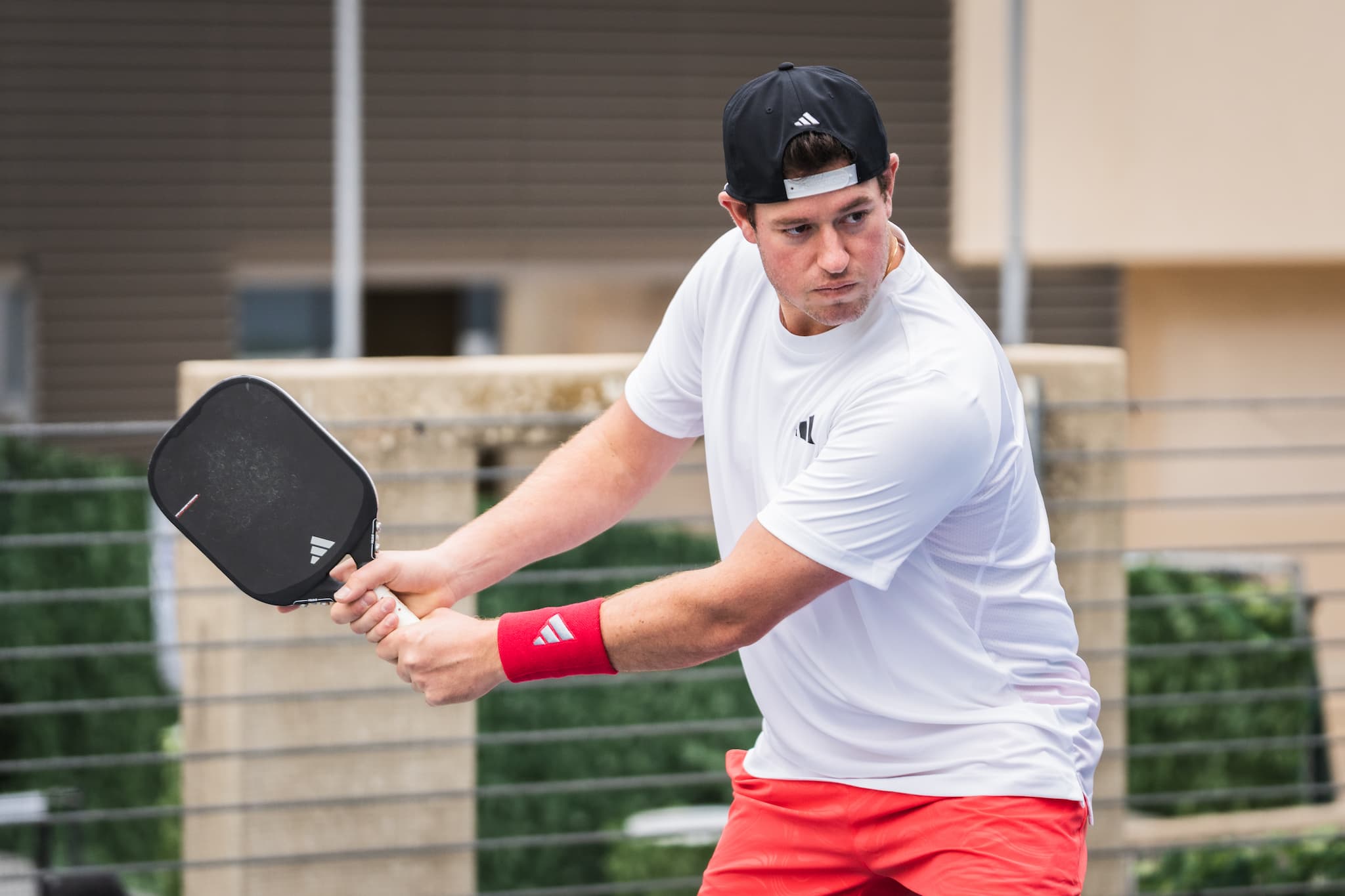 Man playing pickleball wearing a white shirt and red shorts, holding a paddle.