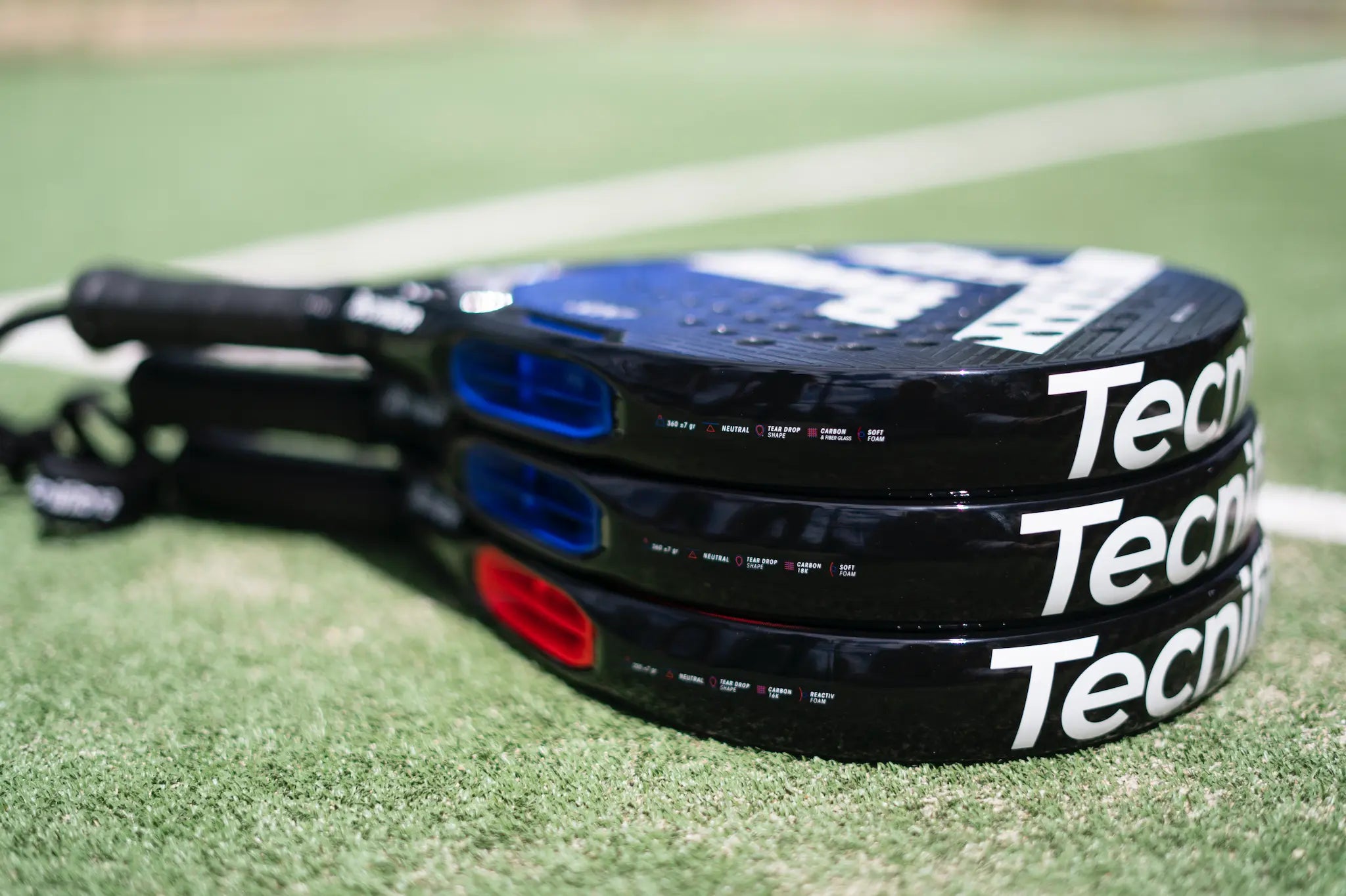 Three black tecnifibre padel rackets on a a padel court.