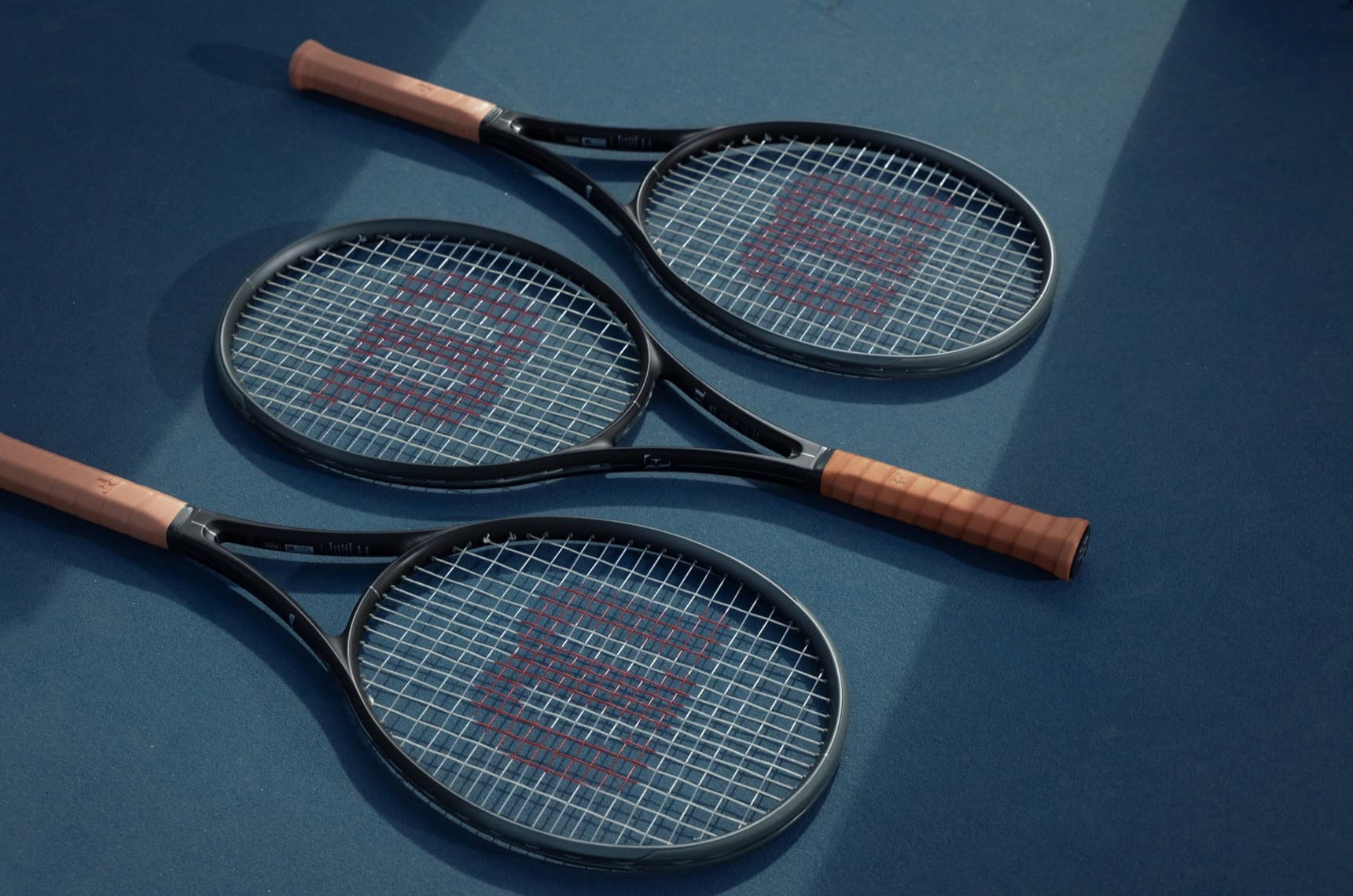 Three tennis rackets with Wilson branding on a blue surface