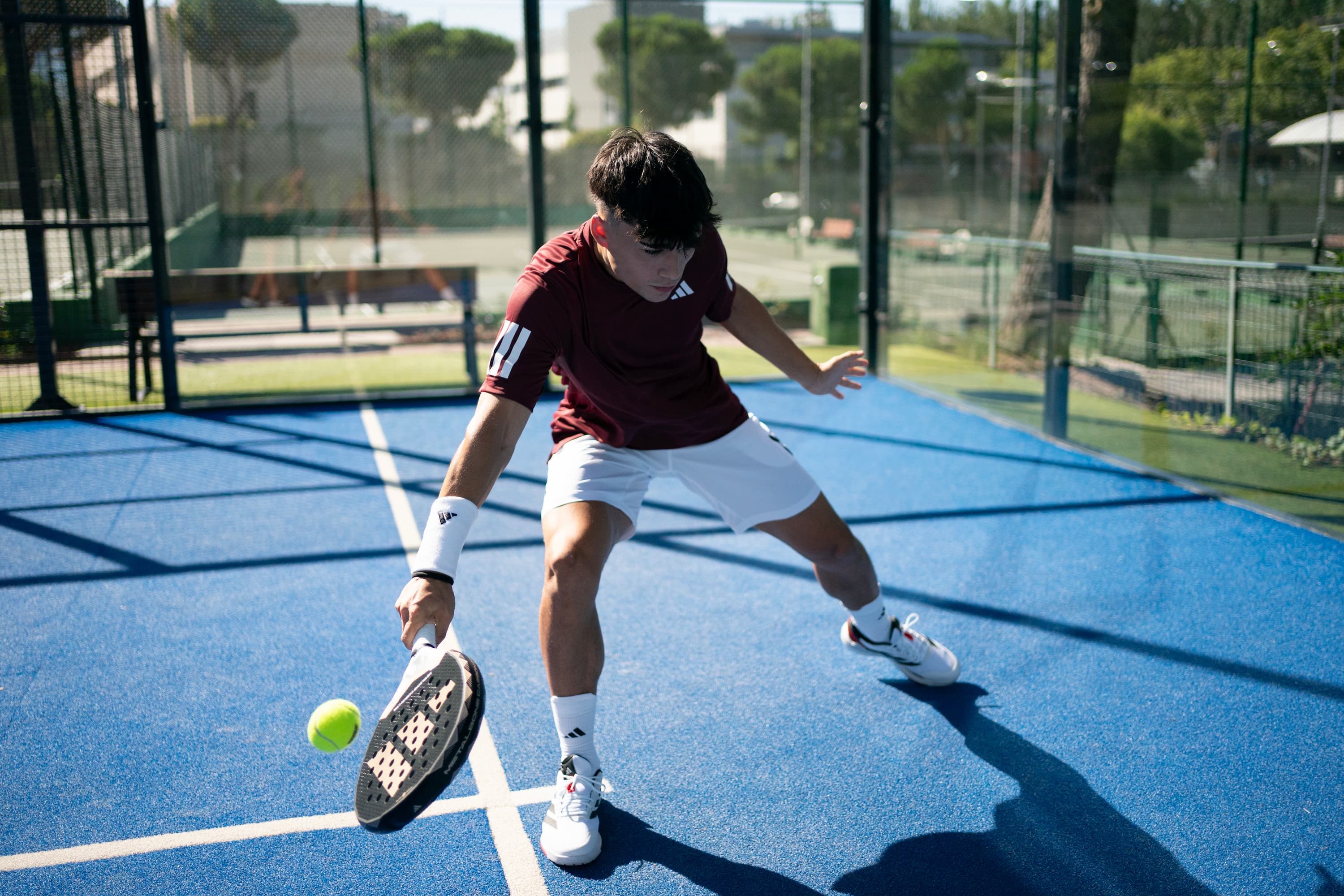 Person playing padel on a blue court with trees and buildings in the background