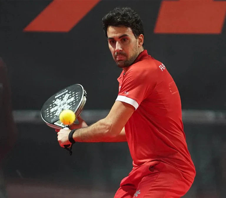 Man in red sports outfit holding a paddle and ball on a tennis court